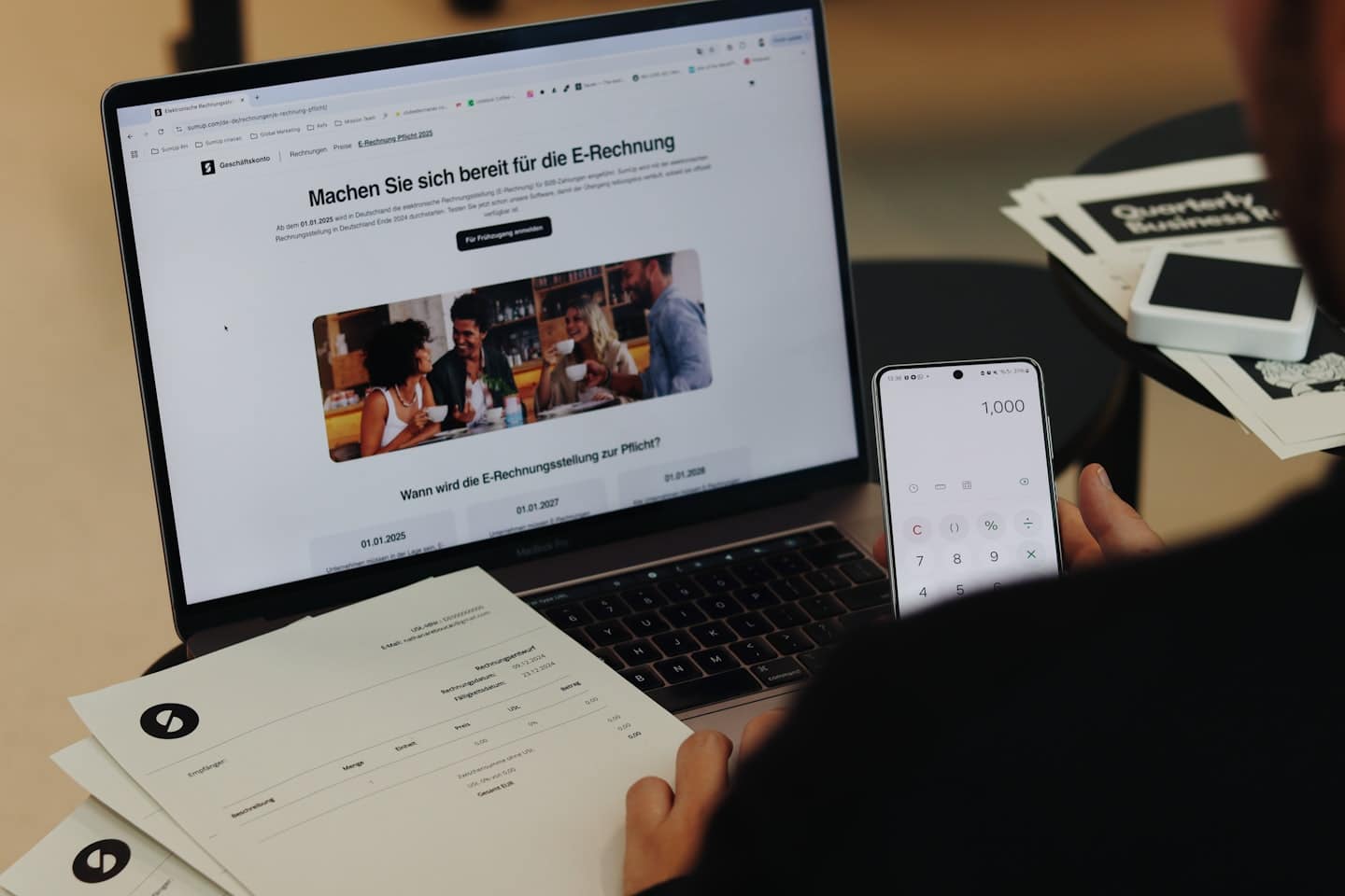 Hands hold a smartphone showing a calculator next to business reports.